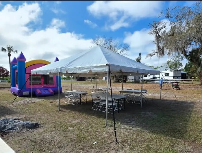 Cape Coral party rentals — white event tent with tables and chairs set up outdoors next to a bounce house